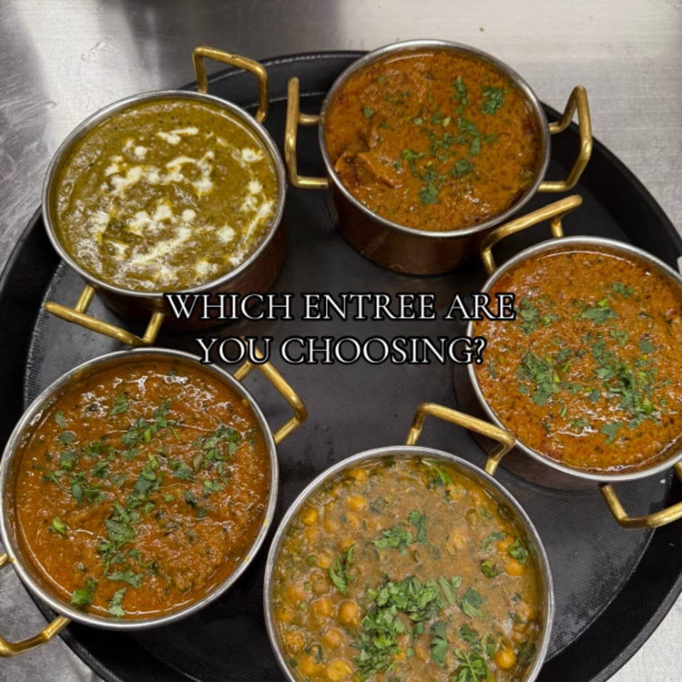 Five Indian curries in brass-handled bowls on a black tray, including green palak paneer and chickpea curry.